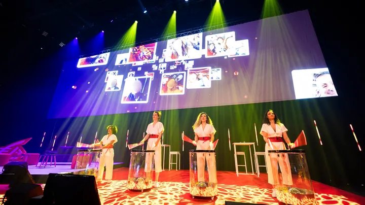 The video of an animated photo mosaic is broadcast live on a giant screen during a company convention.
