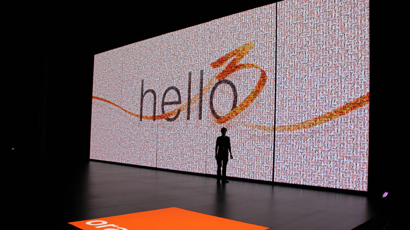 A person in front of the digital photo mosaic created in real time on a giant screen for the Orange Hello! show