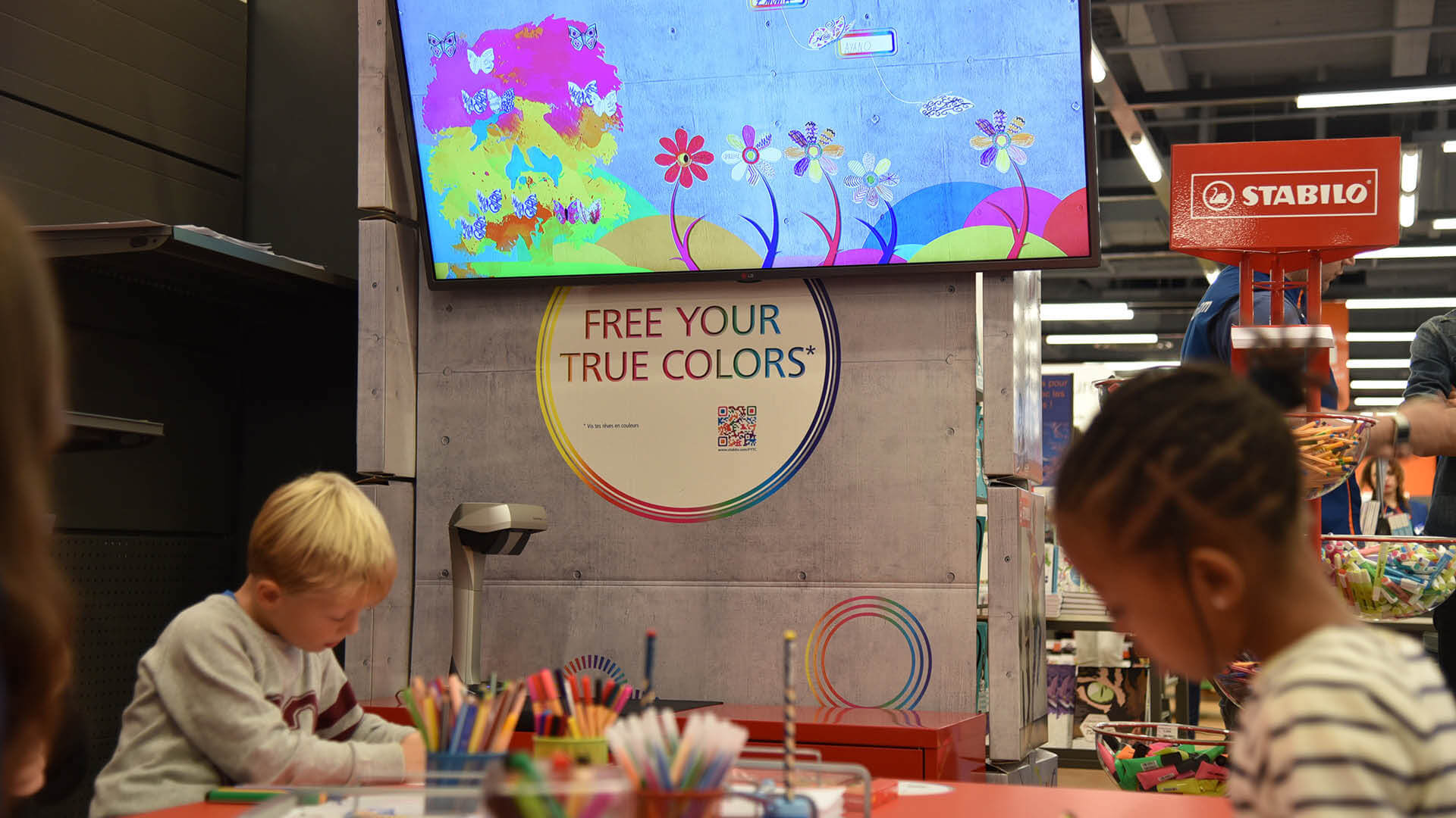 Pendant un événement de Stabilo, des enfants colorient des papillons puis les scannent pour les voir s’animer sur un écran