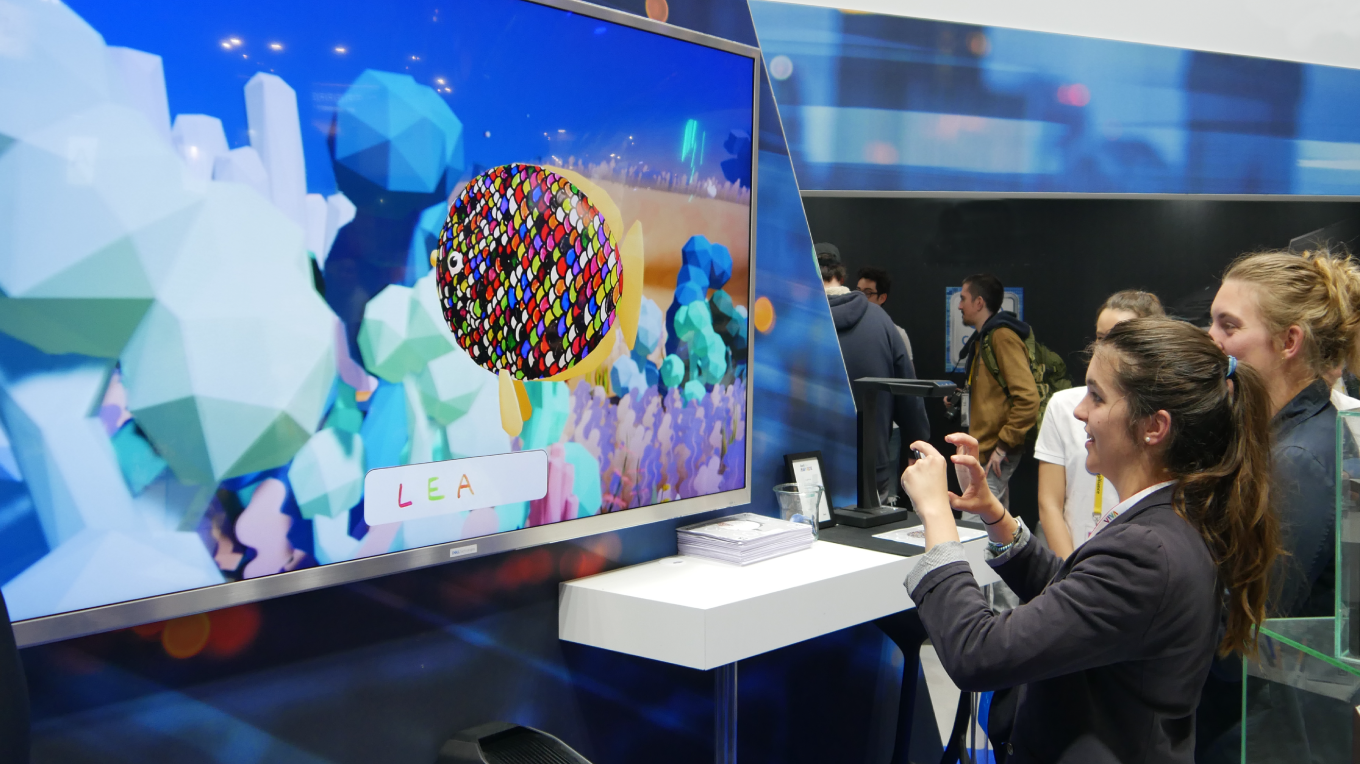 Deux visiteuses devant l'écran de l’animation We Are Colors Ocean Plastic du stand Dell à VivaTech, prenant en photo les poissons qu'elles ont coloriés